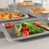 Grey roasting tray with grilled vegetables, chicken, and bread shown in a modern kitchen.