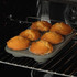Tray of six golden muffins baking in oven, shown in grey non-stick tin