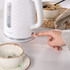 White textured electric kettle, person switching on, beside tea cup and breakfast bowl