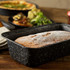 Rectangular cake tin holding a baked loaf dusted with icing sugar, on wooden table.
