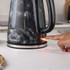 Person switching on black marble-effect electric kettle with illuminated power light