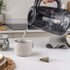 Black marble-effect electric kettle pouring hot water into a grey mug in a kitchen setting