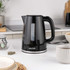 Black electric kettle pouring hot water into grey mug, shown in use for product listing