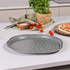 Grey non-stick pizza tray with holes, shown on kitchen counter near fresh tomatoes and herbs