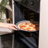 Hand placing homemade pepperoni pizza in oven on round pizza tray