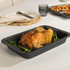 Roast chicken served in a black roasting tin on green vegetables, kitchen table setting