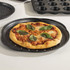 Round margherita pizza with basil leaves shown on black speckled pizza tray