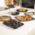 Black speckled non-stick bakeware set shown with assorted baked foods on kitchen counter