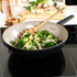Non-stick frying pan on induction hob with stir-fried vegetables and wooden spatula
