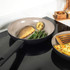 Grey non-stick frying pan on hob with cooked fish, green beans and grilled lemon slice