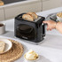 Black two-slice toaster with Salter branding, shown toasting brown bread in a kitchen.