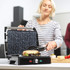 Large electric grill open with a toasted sandwich being removed with tongs on a kitchen counter