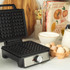 Black and silver electric waffle maker with temperature control dial, closed, side view