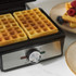 Hand pouring waffle batter into open black electric waffle maker