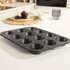 Set of black speckled non-stick bakeware on kitchen counter, includes pizza tray, roasting tray, muffin tin and cake tin.