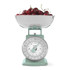Green mechanical kitchen scale with stainless steel bowl of fresh cherries