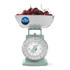 Green mechanical kitchen scale with bowl of cherries, label: no batteries needed