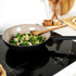 Non-stick wok with stir-fried vegetables on an induction hob, kitchen utensils in background