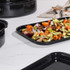 Black enamel roasting tray with mixed roasted vegetables, shown on kitchen worktop