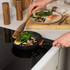 Non-stick frying pan cooking pak choi and mushrooms on induction hob