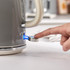 Grey electric kettle close-up, finger pressing illuminated power switch