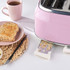 Pink 4-slice toaster with crumb tray extended, next to plate of toast and cup.