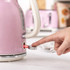 Close-up of hand switching on pink electric kettle, highlighting power lever feature.