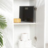 Black bathroom scale with sponge on shelf, three toilet rolls below, white cabinet interior