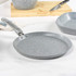 Grey frying pan on induction hob with pancake, stack of pancakes and fruit in background