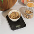 Black digital kitchen scale with ceramic bowl of granola, shown in use for weighing
