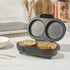 Black electric omelette maker open with cooked omelettes, one being lifted with wooden tongs