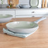 Green non-stick frying pan on wood surface in kitchen, shown from side angle