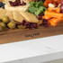 Sliced cheddar cheese with dried cranberries, green olives and pretzels on a wooden board.