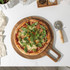 Round acacia wood serving board on kitchen counter with utensils and salt and pepper pots