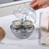 Electric egg cooker in grey with five brown eggs and a finger pressing the power button