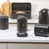 Matte black kitchen storage set on counter, including bread bin, tea, coffee and sugar canisters.