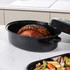 Digital meat thermometer displaying 67.9°C, next to roast lamb in black casserole dish.