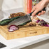 Chef’s knife slicing red onion on wooden Salter chopping board in kitchen.