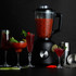 Black blender with jug of red cocktail mix, surrounded by filled cocktail glasses.