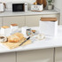 Set of three white kitchen canisters with wood lids, shown with sliced bread and tea bags.