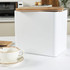 White bread bin with wooden lid, containing a rustic loaf of bread.