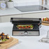 Stainless steel panini press with toasted sandwich, shown open on a kitchen counter.