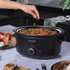 Salter black slow cooker filled with stew, hand adding herbs, on kitchen worktop