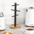 Black and wood mug tree with six pegs for cups, shown on kitchen counter.