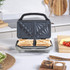 Electric sandwich maker open on kitchen counter, next to plate with toasted sandwich and salad.