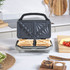 Grey sandwich maker open with two toasted sandwiches inside, shown in a kitchen setting