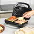Sandwich maker with open lid, two sandwiches being filled with cheese, ham, salami and tomato slices