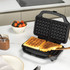 Black waffle maker with two golden waffles on kitchen worktop, hand lifting one waffle.