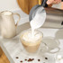 Stainless steel electric milk frother with black handle, shown upright.
