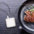 Digital cooking thermometer probe in steak, shown in grill pan